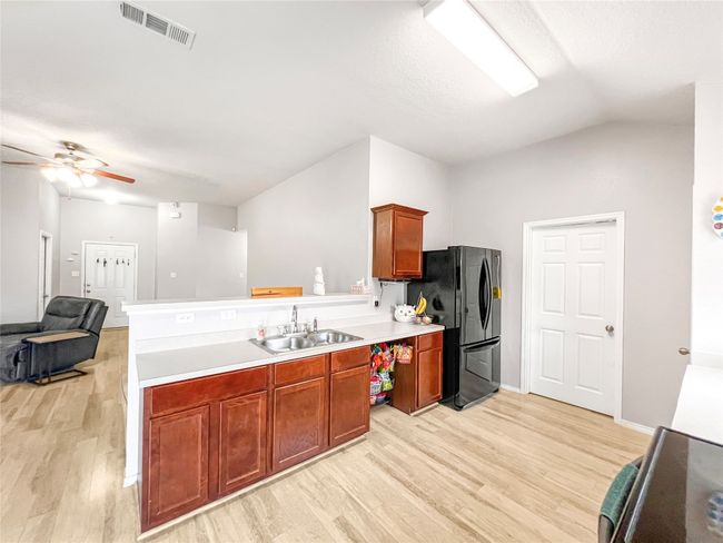 Kitchen with freestanding refrigerator, a sink, light wood finished floors, and lofted ceiling | Image 13