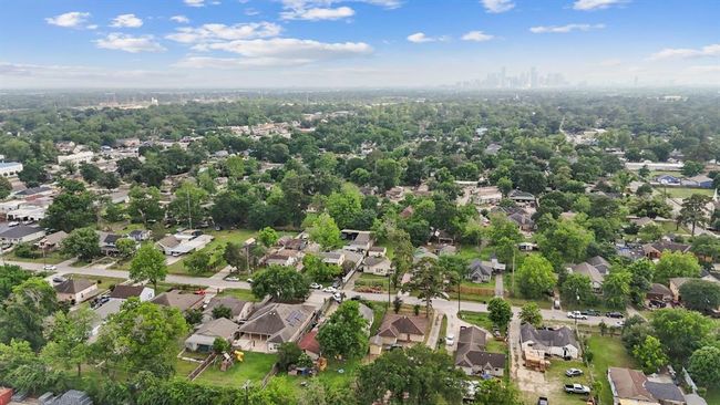 This aerial photo showcases a suburban neighborhood with single-family homes, lush greenery, and a distant city skyline, offering a tranquil living environment within reach of urban amenities. | Image 41