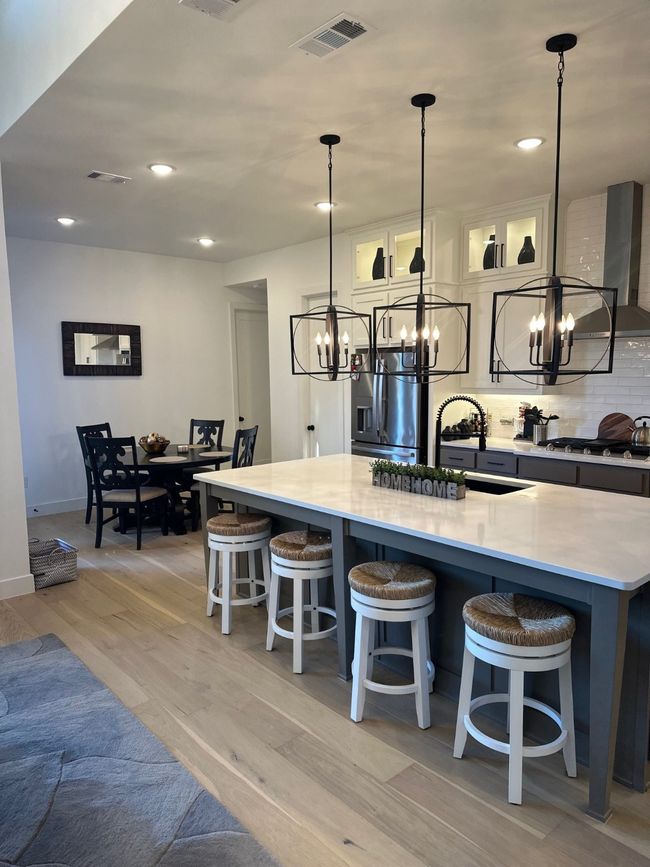 Kitchen with a breakfast bar area, decorative light fixtures, visible vents, light countertops, and glass insert cabinets | Image 15