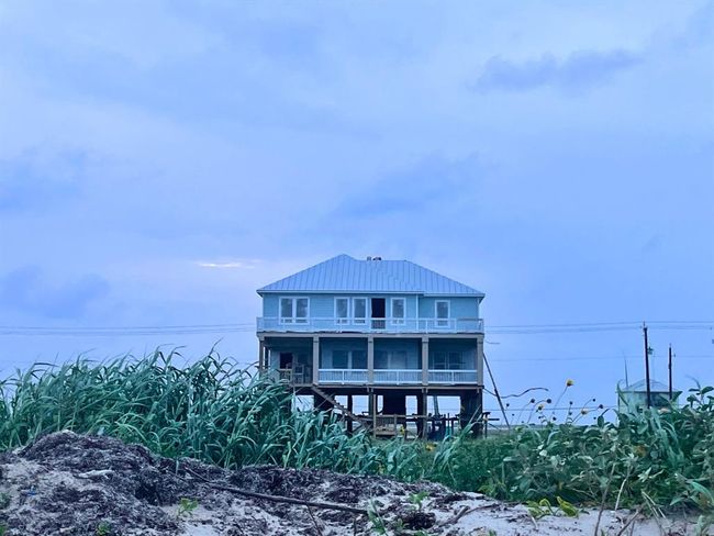 Captured from the protected dunes at dusk, this beach-facing view of the home showcases its imposing elevation, expansive glass windows, and peaceful presence. It’s not just beachfront—it’s a front-row seat to sunrises, stargazing, and serenity. | Image 7