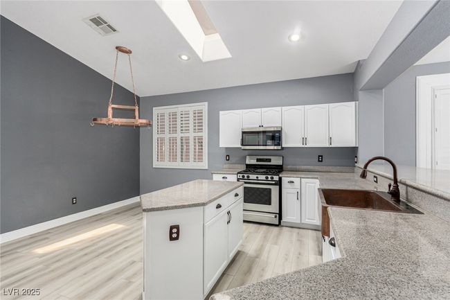 Kitchen, white cabinetry, light stone counters, copper sink, and appliances with stainless steel finishes | Image 10