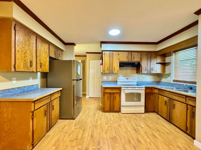 Kitchen featuring white range with electric stovetop, under cabinet range hood, freestanding refrigerator, ornamental molding, and brown cabinets | Image 5