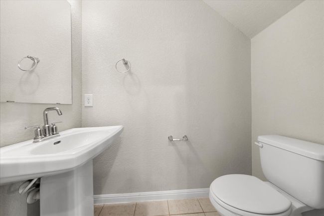 Half bath featuring toilet, tile patterned flooring, vaulted ceiling, baseboards, and a sink | Image 14