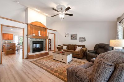 Living room with light wood-type flooring, a stone fireplace, ceiling fan, and high vaulted ceiling | Image 3