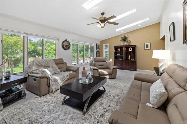Living room with ceiling fan, carpet flooring, and lofted ceiling with skylight | Image 9