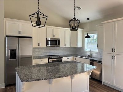 Kitchen with stainless steel appliances, white cabinets, a center island, and dark wood-type flooring | Image 3