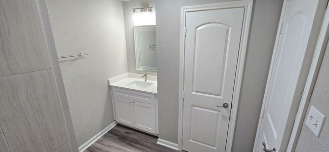 Modern hall bathroom with a single vanity sink, a framed mirror, and neutral wall tones. The room features a white paneled door to a spacious linen closet and vinyl plank flooring, creating a clean and contemporary look. | Image 15