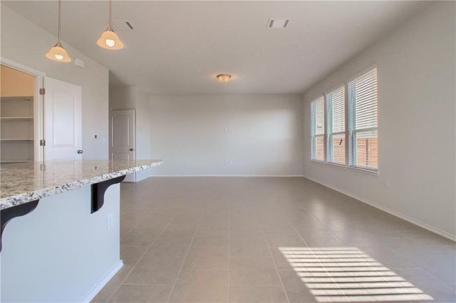 Kitchen with light tile patterned floors, decorative light fixtures, a kitchen breakfast bar, light stone countertops, and baseboards | Image 15