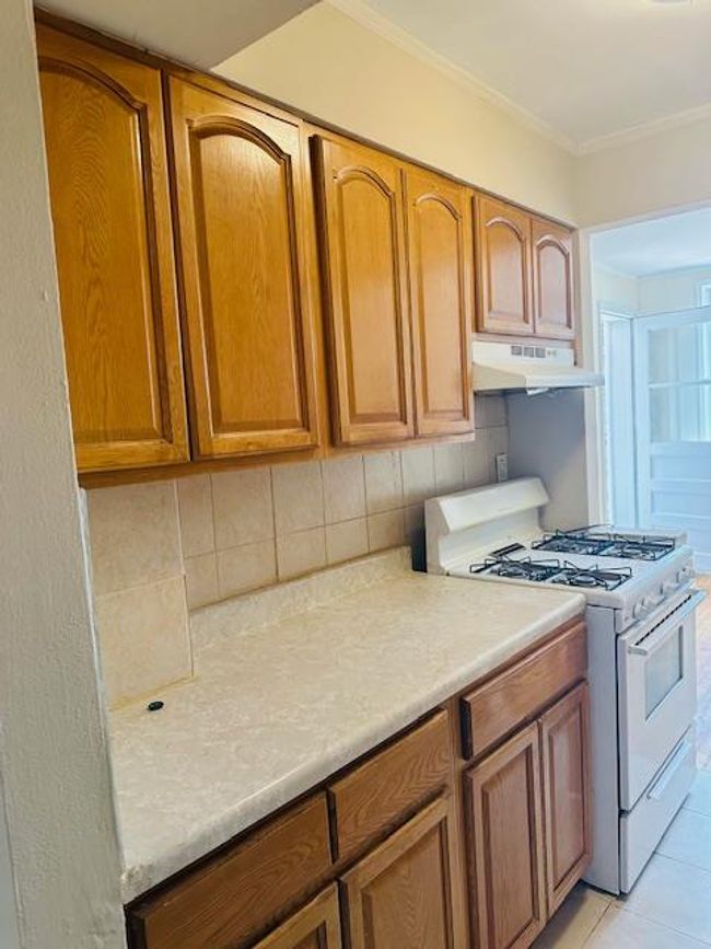 Kitchen featuring white gas range oven, under cabinet range hood, decorative backsplash, light countertops, and brown cabinetry | Image 11