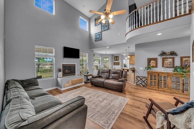 Living room featuring a high ceiling, a ceiling fan, a glass covered fireplace, and light wood-type flooring | Image 13