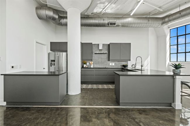 Kitchen with gray cabinets, wall chimney range hood, dark countertops, high quality fridge, and a sink | Image 11
