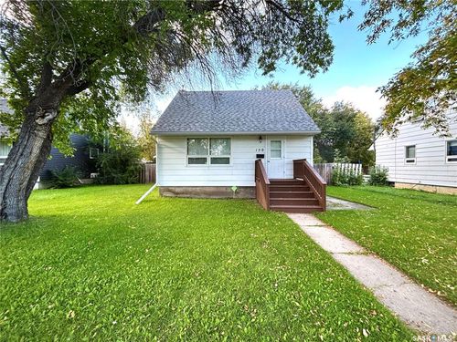 White siding exterior with a dark shingle roof, complemented by a concrete walkway and wooden steps | Card Image
