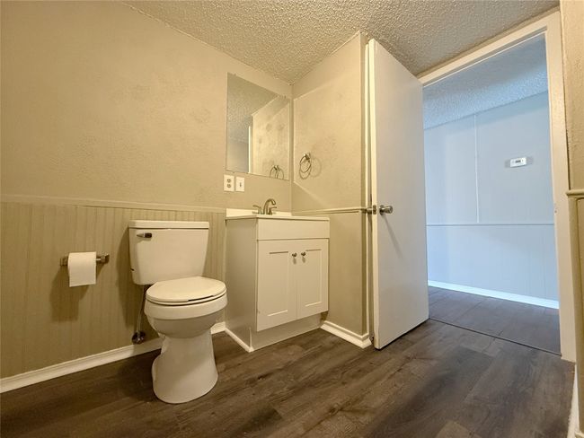 Half bath featuring a textured ceiling, wood finished floors, toilet, and wainscoting | Image 9
