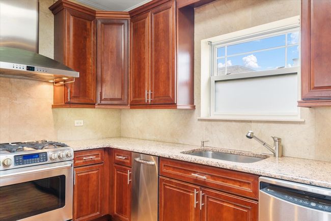 Kitchen featuring light stone counters, tasteful backsplash, appliances with stainless steel finishes, a sink, and wall chimney range hood | Image 6