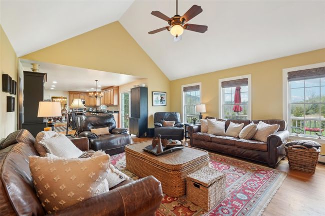 Living room with high vaulted ceiling, a wealth of natural light, light wood-style floors, and ceiling fan with notable chandelier | Image 9