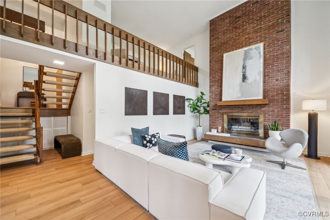 Living area featuring hardwood / wood-style floors, a towering ceiling, visible vents, a brick fireplace, and stairs | Image 20