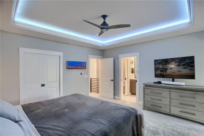 This luxurious primary bedroom features a tray ceiling with ambient LED lighting, a statement fan, and elegant tufted furnishings that create a serene, spa-like retreat. | Image 29