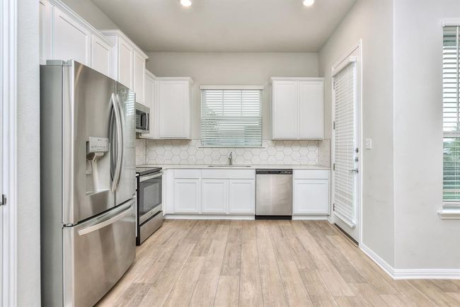 Kitchen featuring appliances with stainless steel finishes, light countertops, white cabinets, and light wood-type flooring | Image 8