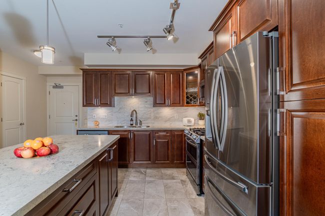 Kitchen with stainless steel appliances, a sink, backsplash, light stone counters, and glass insert cabinets | Image 18