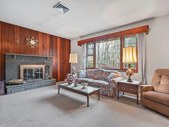 Carpeted living room featuring a stone fireplace and wood walls | Image 11