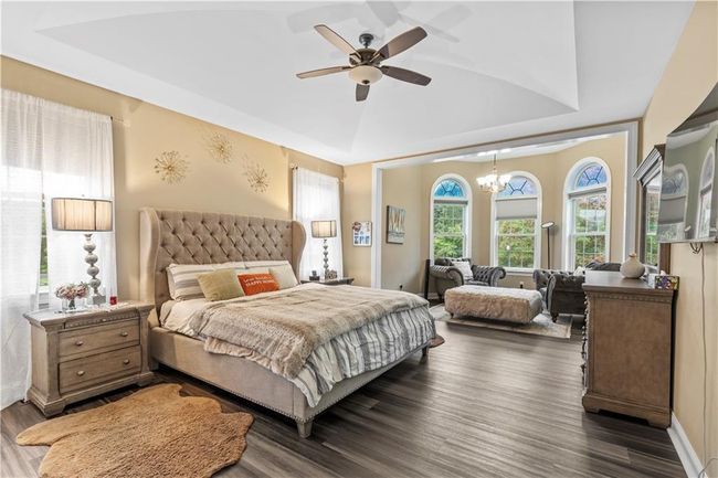 Bedroom with dark wood finished floors, a chandelier, ceiling fan, and a raised ceiling | Image 17