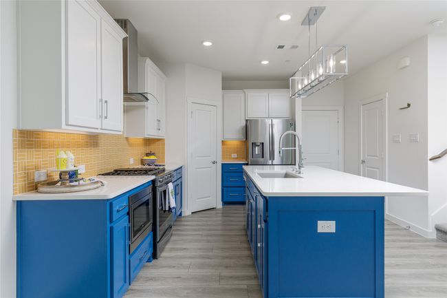 Kitchen featuring blue cabinetry, wall chimney range hood, light wood-style floors, light countertops, and appliances with stainless steel finishes | Image 10