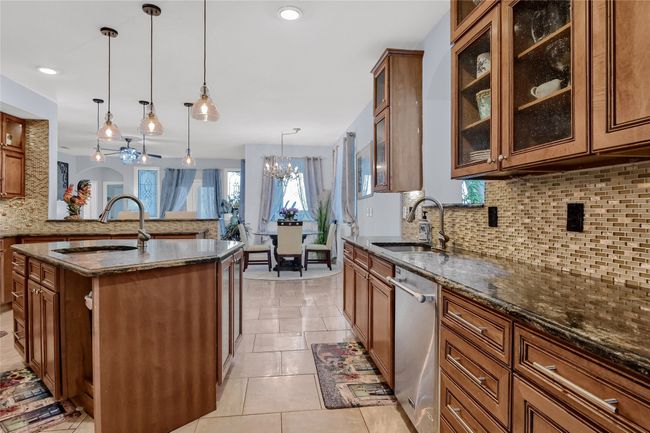 Kitchen featuring backsplash, stainless steel dishwasher, a center island with sink, a chandelier, and hanging light fixtures | Image 14