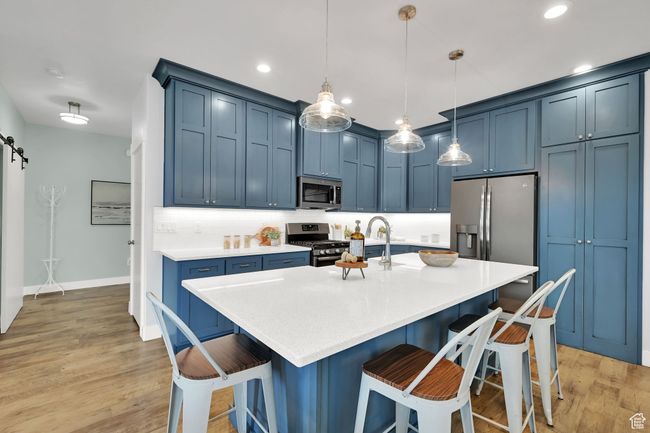 Kitchen with appliances with stainless steel finishes, blue cabinetry, light wood-style flooring, light countertops, and a kitchen bar | Image 9