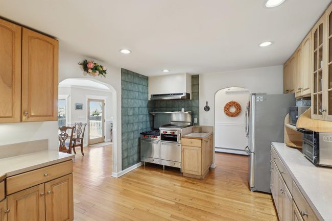 Kitchen featuring arched walkways, under cabinet range hood, light wood-type flooring, and appliances with stainless steel finishes | Image 14