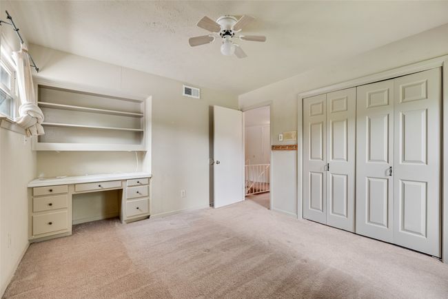 Unfurnished bedroom featuring light colored carpet, an office area, a closet, a ceiling fan, and baseboards | Image 19