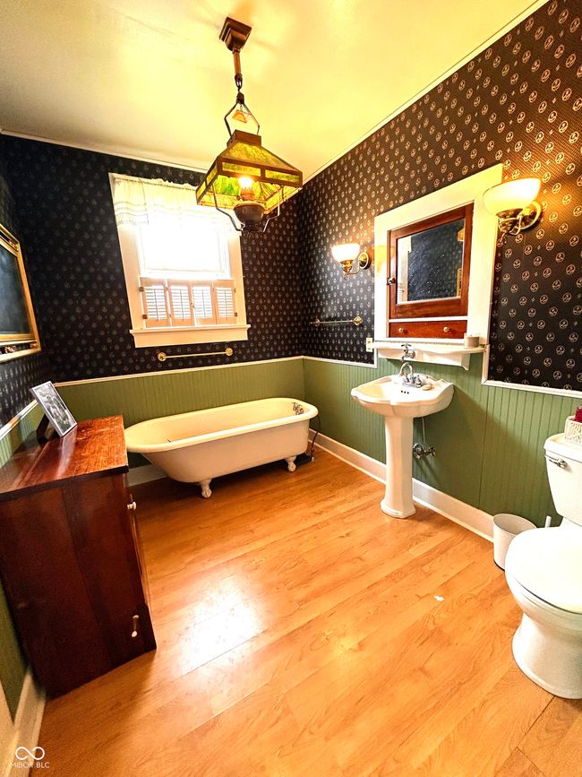 bathroom with wood finished floors, wallpapered walls, a freestanding tub, a wainscoted wall, and toilet | Image 24