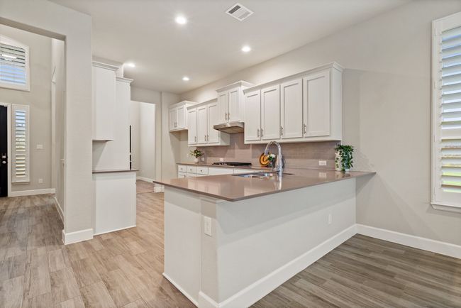 Kitchen with under cabinet range hood, light wood-style floors, backsplash, a peninsula, and white cabinets | Image 8