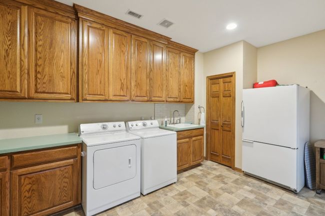 Laundry area featuring washing machine and clothes dryer, visible vents, a sink, and cabinet space | Image 19
