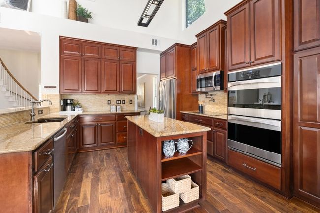 Kitchen with stainless steel appliances, decorative backsplash, light stone counters, open shelves, and a towering ceiling | Image 10