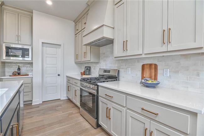 Kitchen featuring light hardwood / wood-style flooring, tasteful backsplash, premium range hood, black microwave, and stainless steel range with gas stovetop | Image 18