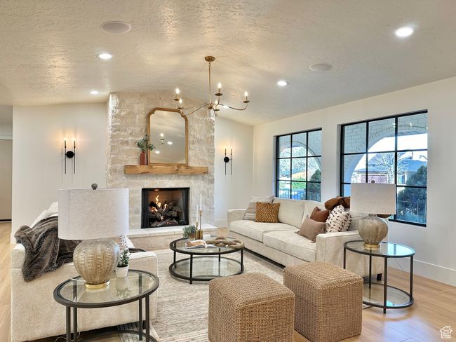 Living area with light wood finished floors, a textured ceiling, recessed lighting, a stone fireplace, and a chandelier | Image 6