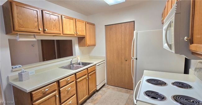 Kitchen with white appliances, a sink, light countertops, stone finish floors, and brown cabinetry | Image 8