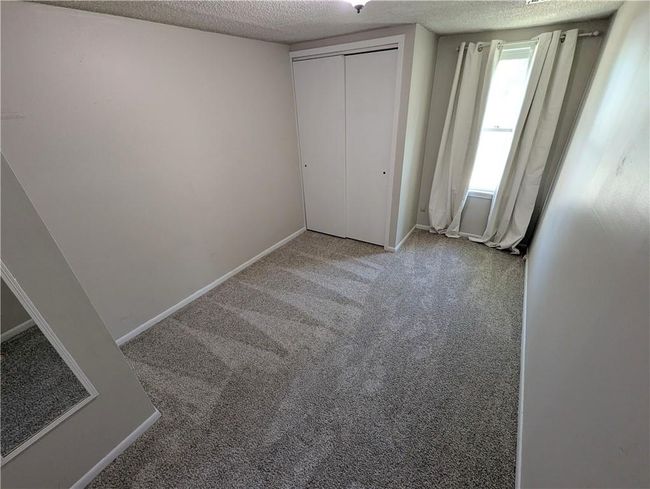 Unfurnished bedroom with a textured ceiling, carpet, baseboards, and a closet | Image 14