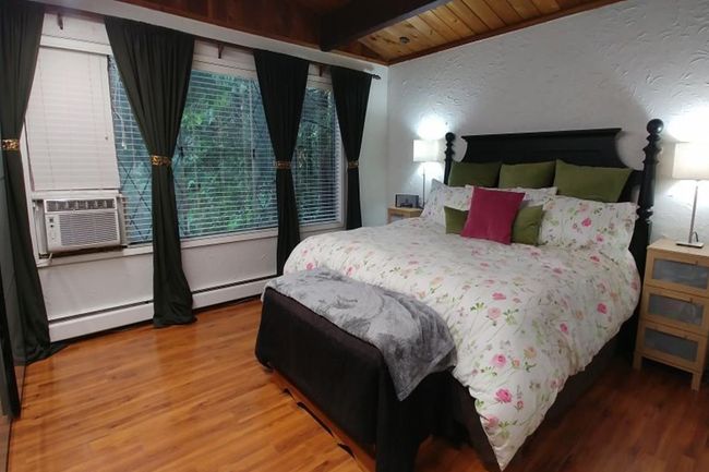 Bedroom featuring a textured wall, wood finished floors, baseboard heating, cooling unit, and beam ceiling | Image 11