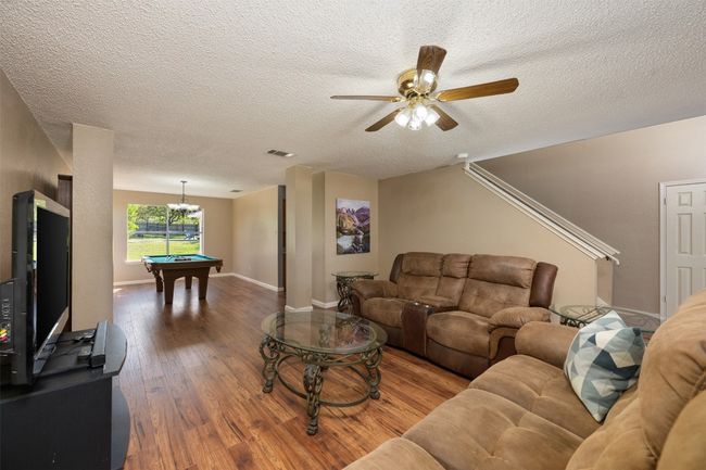 Living room featuring pool table, a textured ceiling, a ceiling fan, visible vents, and wood finished floors | Image 7