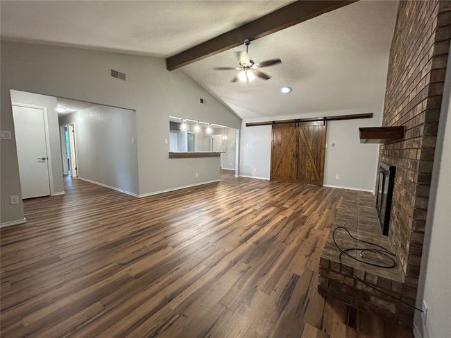 Unfurnished living room with ceiling fan, dark wood-style flooring, a brick fireplace, a barn door, and recessed lighting | Image 9