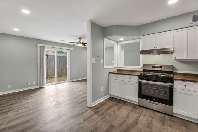 Kitchen with gas range, under cabinet range hood, dark countertops, a ceiling fan, and dark wood-type flooring | Image 7
