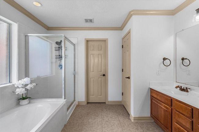 This bathroom features a spacious layout with a glass-enclosed shower, a separate bathtub, dual sinks with wooden cabinetry, and neutral tile flooring. It offers a clean and bright atmosphere with natural light from a frosted window. | Image 27