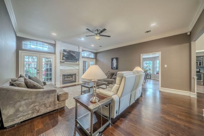 Living room featuring ceiling fan, crown molding, a large fireplace, dark wood finished floors, and french doors. Access to outdoor covered patio area | Image 7