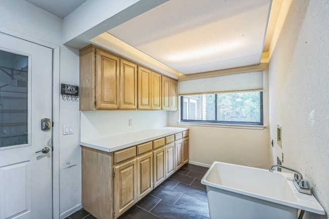 Clothes washing area with a sink, a textured wall, cabinet space, and baseboards | Image 17