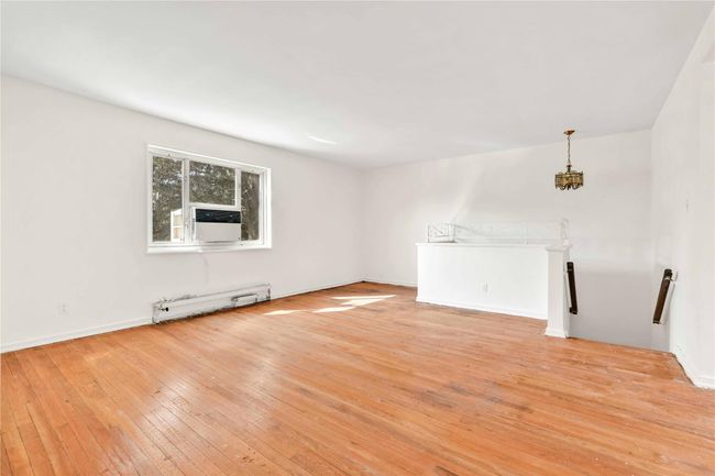 Unfurnished living room with a baseboard radiator, light wood-type flooring, cooling unit, and a chandelier | Image 12