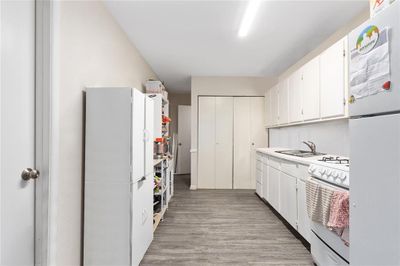 Kitchen featuring white appliances, sink, light wood-type flooring, and white cabinetry | Image 3