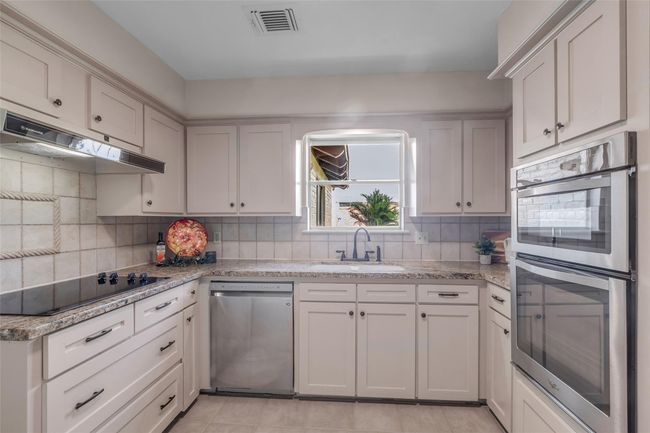 This kitchen features modern stainless steel appliances, granite countertops, and ample cabinetry. A window above the sink provides natural light, creating a bright and welcoming space. | Image 19