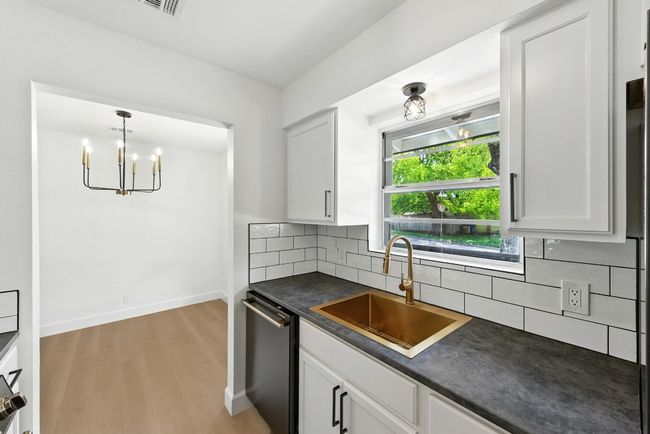 Kitchen with dark countertops, backsplash, light wood-type flooring, white cabinets, and dishwashing machine | Image 14