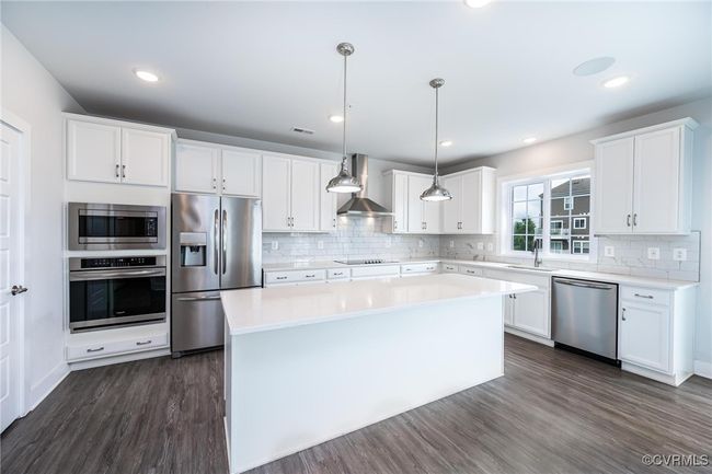 Kitchen with appliances with stainless steel finishes, wall chimney exhaust hood, dark wood-type flooring, a kitchen island, and white cabinets | Image 8